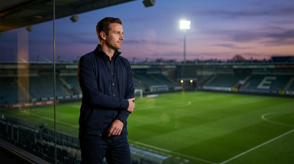 Jordan Galtier : l’ascension d’un tacticien au Toulouse FC Jordan Galtier, entraîneur, regarde un stade de football vide depuis une loge vitrée au crépuscule.